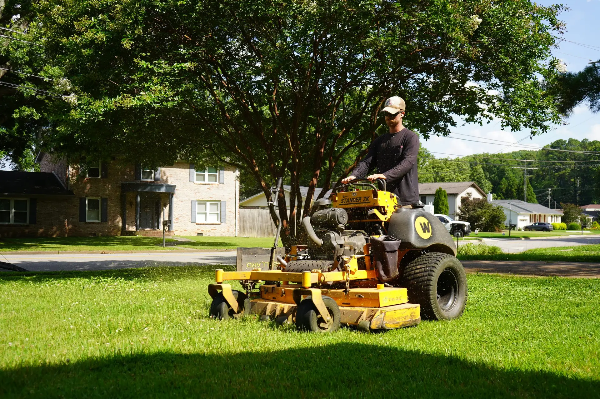Olympic Mountain Landscaping crew member mowing a residential front lawn with a commercial stand-on mower in North Alabama