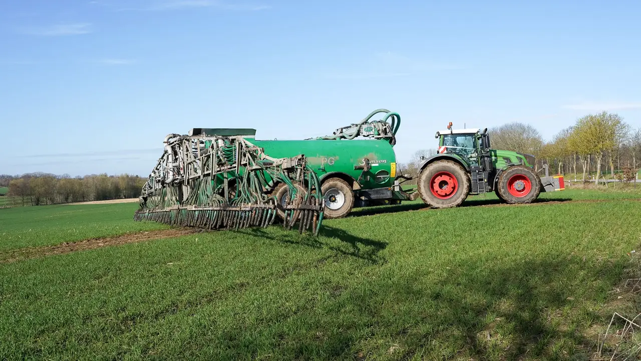 Broadcast spreader applying granular fertilizer across a healthy green North Alabama lawn