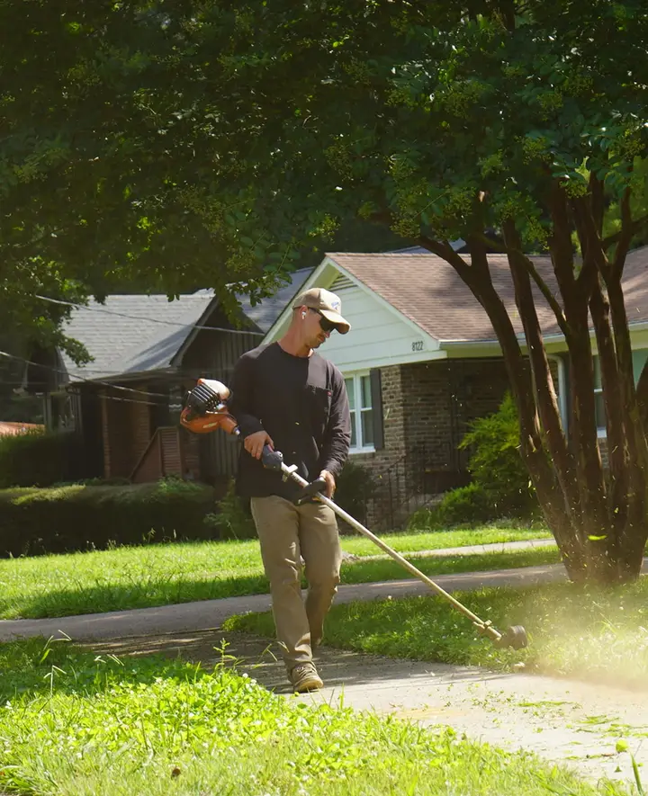 Olympic Mountain Landscaping crew member edging a driveway with a string trimmer during a lawn care visit at a North Alabama home
