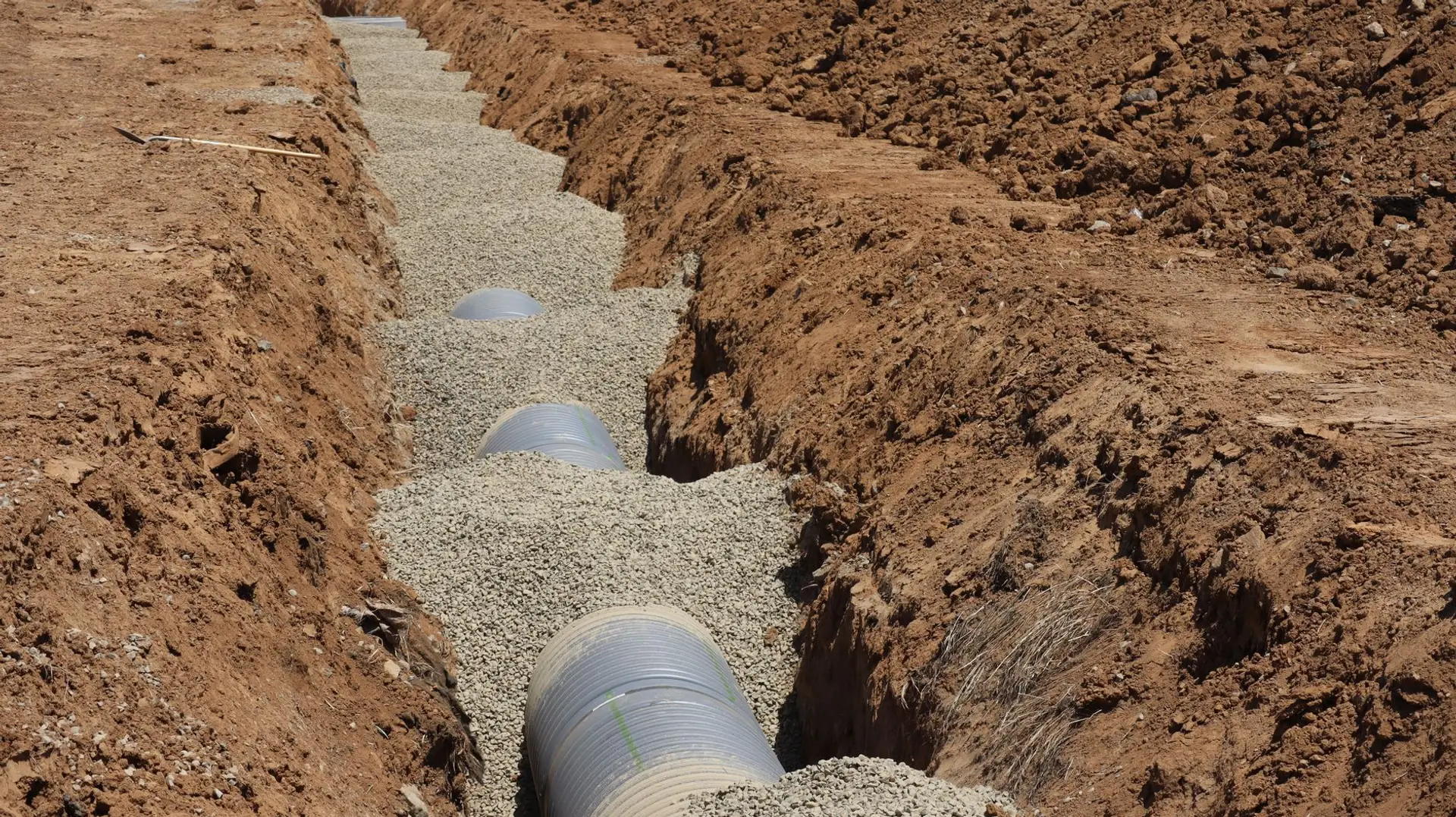 A drainage pipe set in gravel inside a freshly dug trench