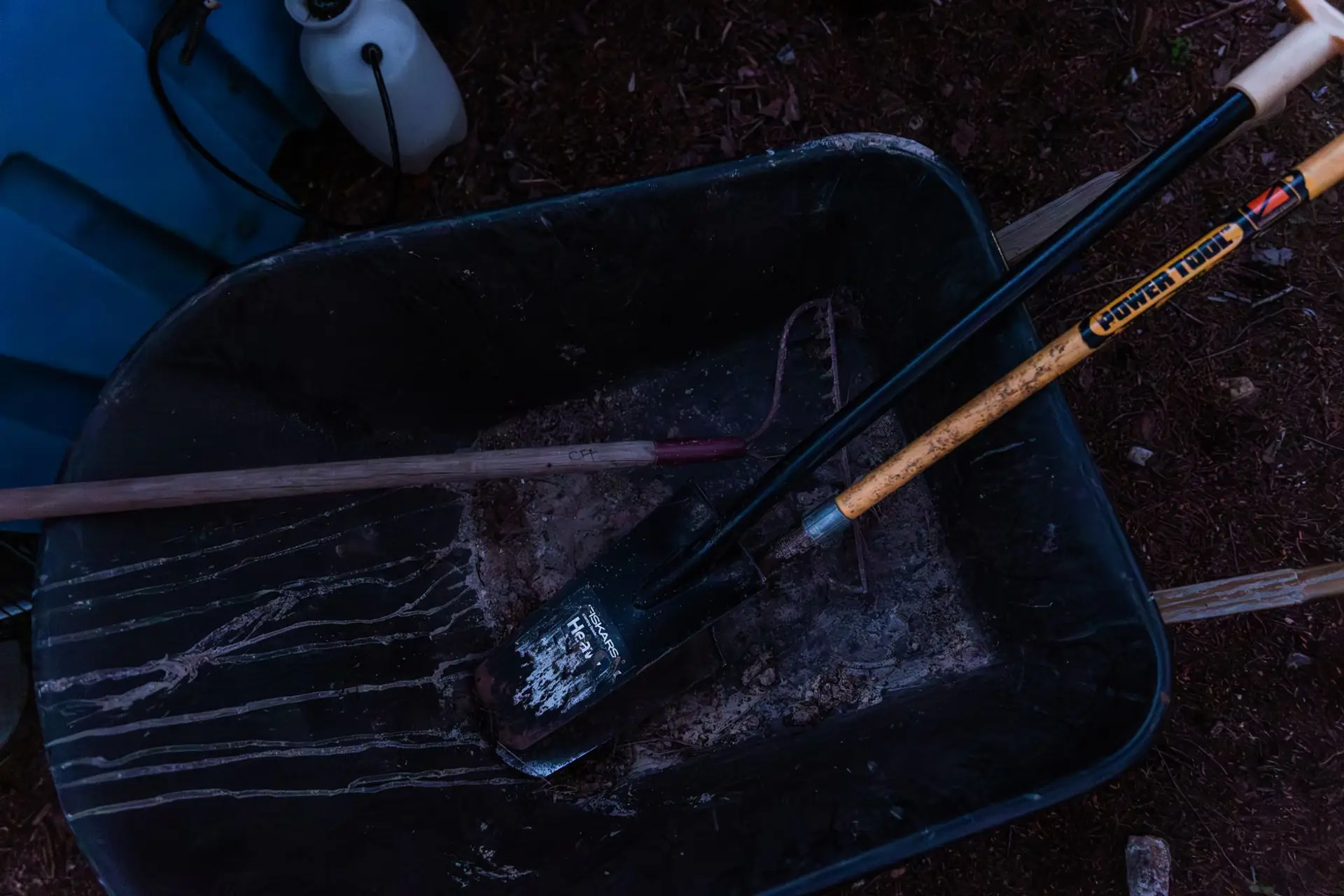 A wheelbarrow with a shovel and rake set on dark mulch during a bed cleanout